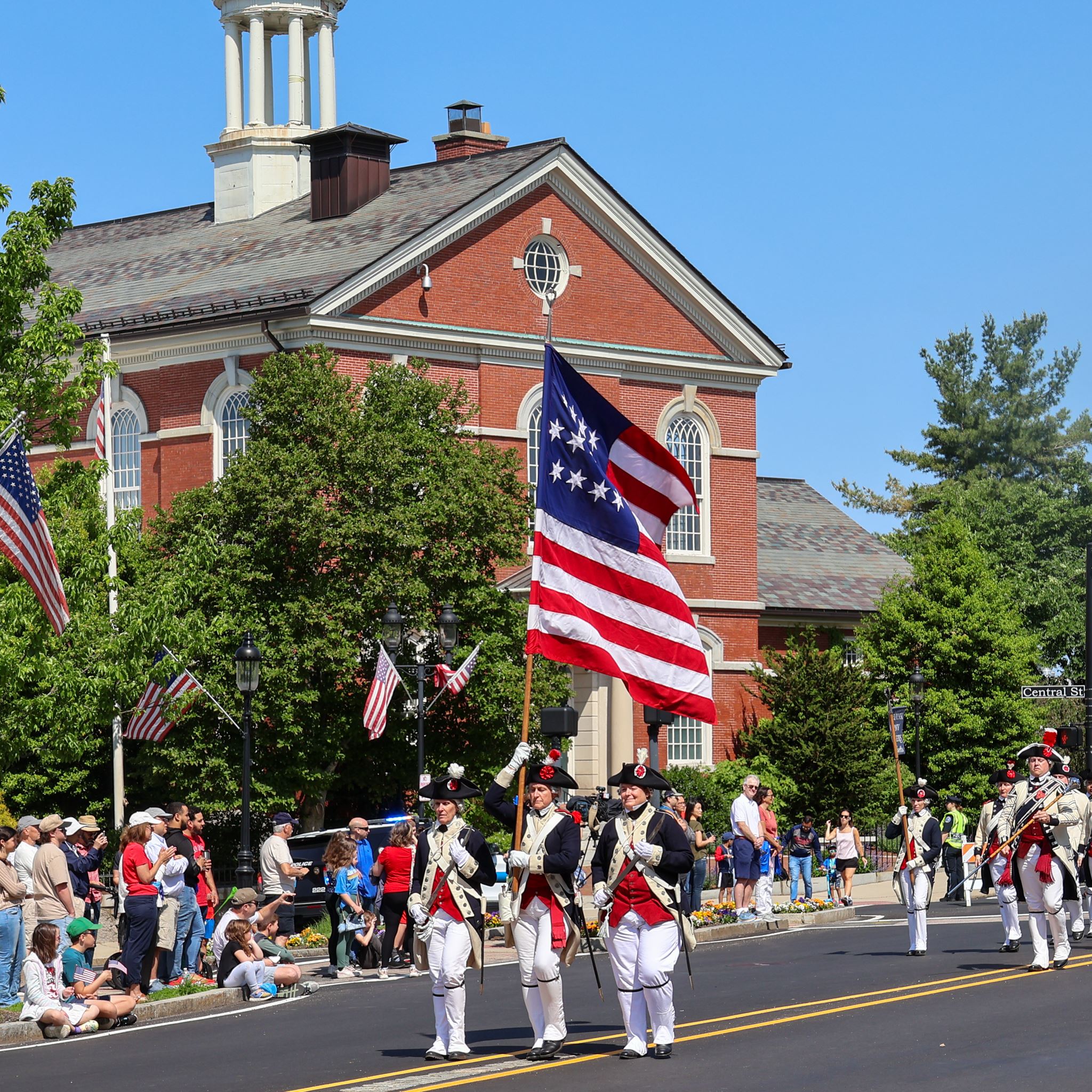 People in colonial military uniforms marching in front of the library