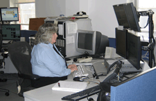 A woman sitting at a computer with several monitors.